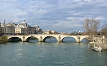 Steinerne Pont Royal mit fünf Bögen über der Seine vor dem Musée d’Orsay, ruhiges Wasser und winterliche Bäume.