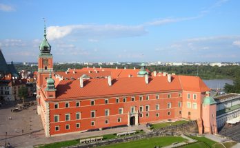 Luftblick auf das Königsschloss in Warschau mit roten Dächern und der Weichsel im Hintergrund.
