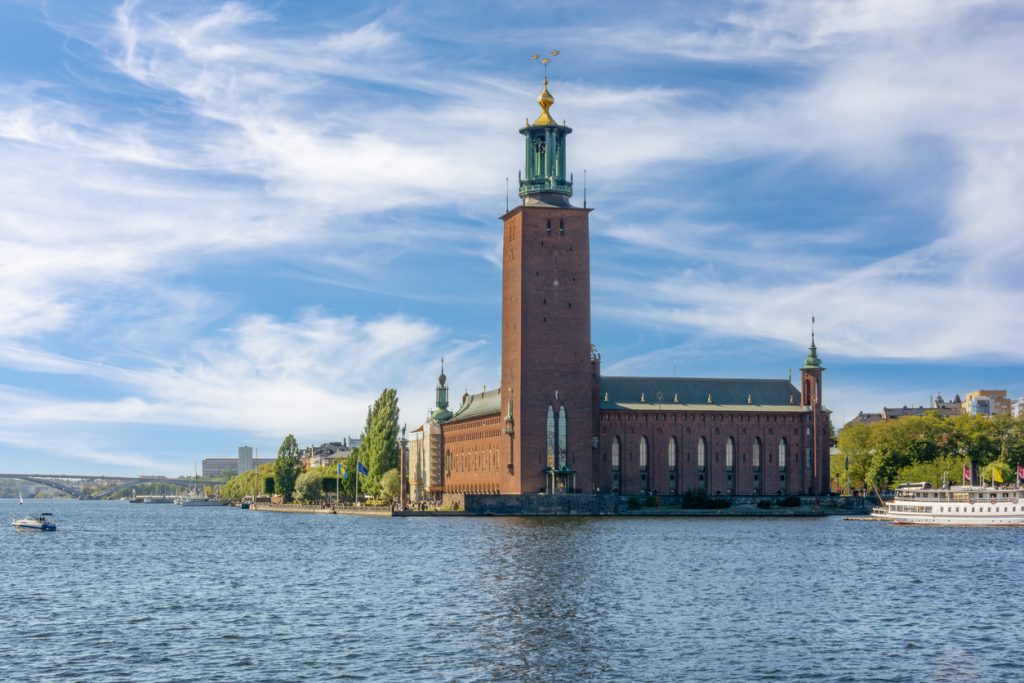 Stockholms Stadshuset am Wasser mit hohem Backsteinturm und vorbeifahrenden Booten.