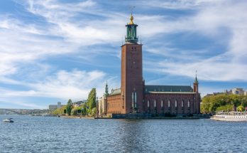 Stockholms Stadshuset am Wasser mit hohem Backsteinturm und vorbeifahrenden Booten.