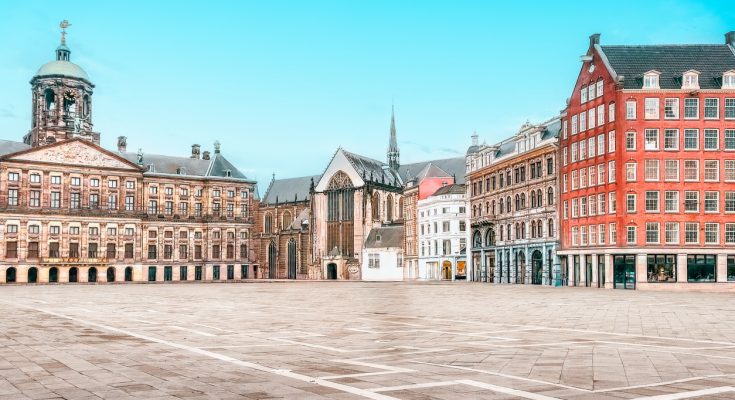 Weitwinkelfoto des leeren Damplatzes mit dem Königlichen Palast links, der Nieuwe Kerk in der Mitte und historischen Giebelhäusern rechts.