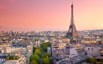 Blick über Pariser Dächer mit dem Eiffelturm rechts im Bild unter rosa Abendhimmel.