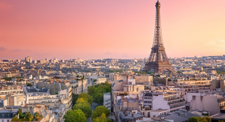 Blick über Pariser Dächer mit dem Eiffelturm rechts im Bild unter rosa Abendhimmel.