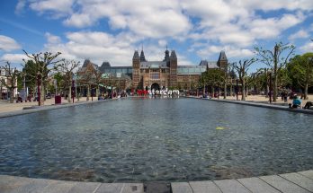 Frontansicht des Rijksmuseums mit langem Wasserbecken und Besuchern auf dem Museumplein.
