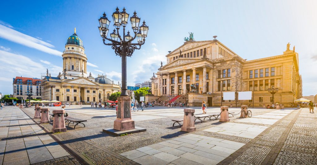 Weitwinkelaufnahme des Gendarmenmarkts mit dem Konzerthaus Berlin und dem Französischen Dom bei Sonnenschein.