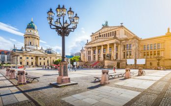 Weitwinkelaufnahme des Gendarmenmarkts mit dem Konzerthaus Berlin und dem Französischen Dom bei Sonnenschein.