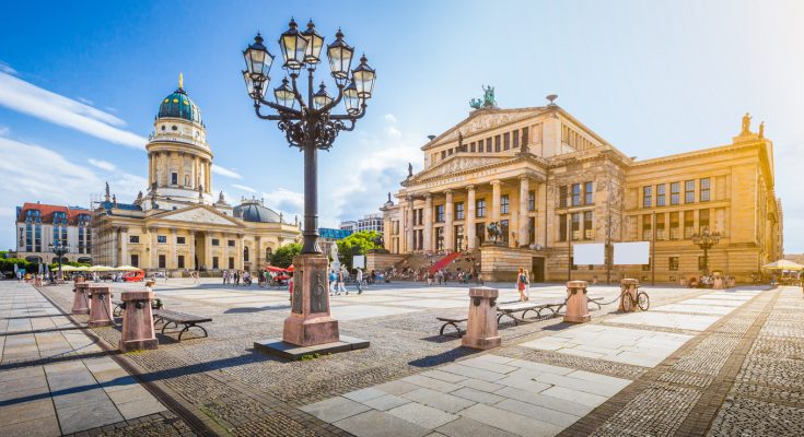 Weitwinkelaufnahme des Gendarmenmarkts mit dem Konzerthaus Berlin und dem Französischen Dom bei Sonnenschein.