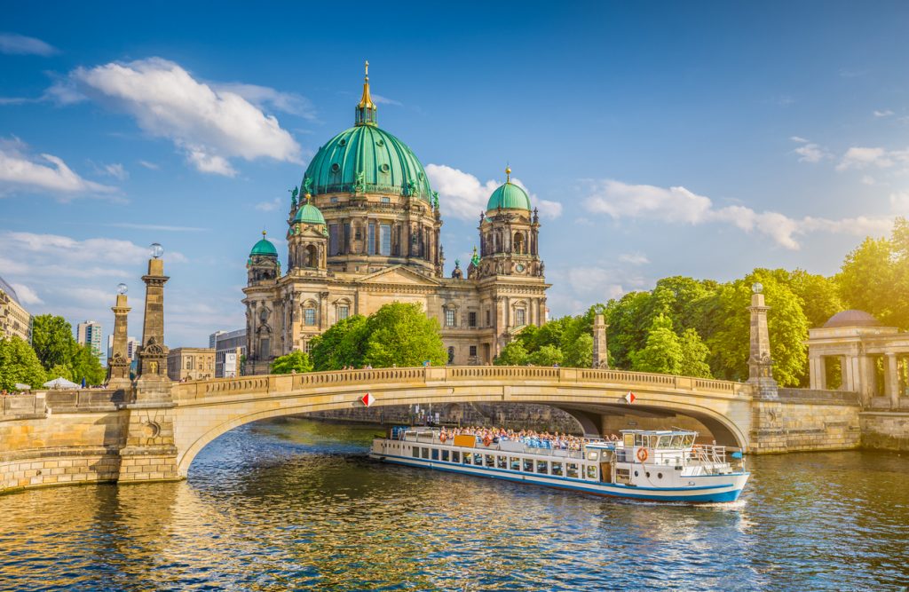 Berliner Dom auf der Museumsinsel mit Ausflugsschiff auf der Spree und steinerner Brücke im Vordergrund.