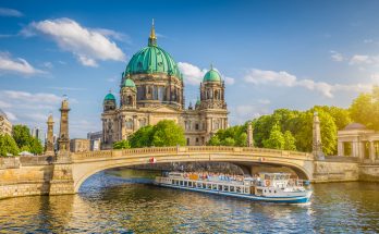 Berliner Dom auf der Museumsinsel mit Ausflugsschiff auf der Spree und steinerner Brücke im Vordergrund.