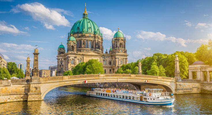 Berliner Dom auf der Museumsinsel mit Ausflugsschiff auf der Spree und steinerner Brücke im Vordergrund.